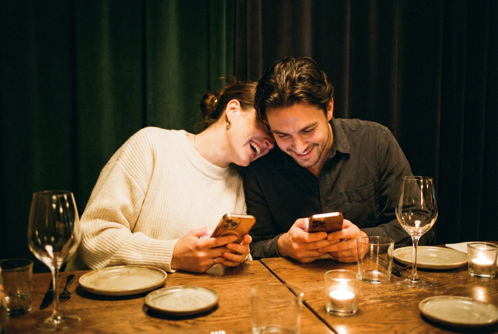 Two guests at a candlelit dinner reviewing their bill on their phones together